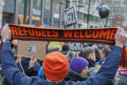 A demonstrator holds up a scarf reading 'Refugees welcome'.